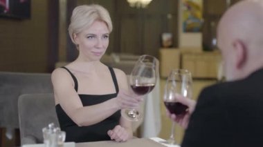 Muhteşem sarışın kadın restoranda bir adamla kadeh tokuşturup kırmızı şarap içiyor. Kafe 'de kel bir kocayla romantik bir akşam yemeği yiyen güzel beyaz kadın portresi. Aşk, aşk.