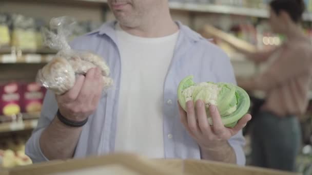 Неузнаваемый человек, стоящий в продуктовом с капустой и пряничным печеньем. Взрослый кавказский покупатель выбирает здоровую и нездоровую пищу. Покупка, образ жизни, диета . — стоковое видео