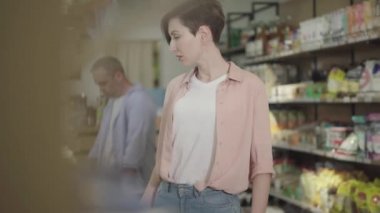 Genç ve çekici bir kadın markete bakıyor ve kurabiye paketlerini çalıyor. Yiyecek dükkanında kadın soyguncunun portresi. Suç, hırsızlık, soygun, yaşam tarzı.