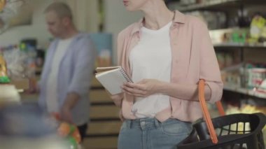 Alışveriş listesi olan tanınmayan bir kadın marketten alışveriş yapıyor. Genç beyaz kadın alıcı ürünleri alıyor ve alışveriş sepetiyle gidiyor. Satın alma, tüketim, yaşam tarzı..