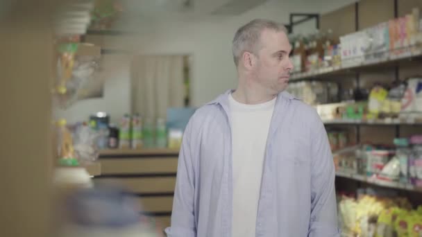 Caucasian man looking around and hiding packaging of cookies in shirt. Adult confident robber stealing product in grocery and leaving. Industry safety, crime, robbery, lifestyle, violation of law. — Stock Video