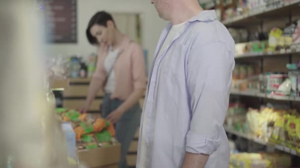 Hombre adulto irreconocible robando galletas en el mercado de alimentos. Ladrón caucásico tomando embalaje y marchándose. Mujer eligiendo bienes en el fondo. Crimen, violación de la ley, robo, estilo de vida . — Vídeos de Stock