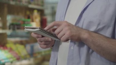 Not defterinde tanınmayan yetişkin adam alışveriş listesini kontrol ediyor. Bakkaldan ürün alan erkek müşterinin yan görüntüsü. Tüketim, yaşam tarzı, sağlıklı beslenme, diyet.
