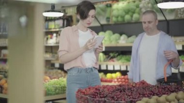 Pozitif beyaz erkek ve kadının el ele tutuşması süpermarket rafından çilek alıyormuş gibi. Marketten yiyecek alan gülen erkek ve kadın müşterinin portresi. Yaşam tarzı, flört..