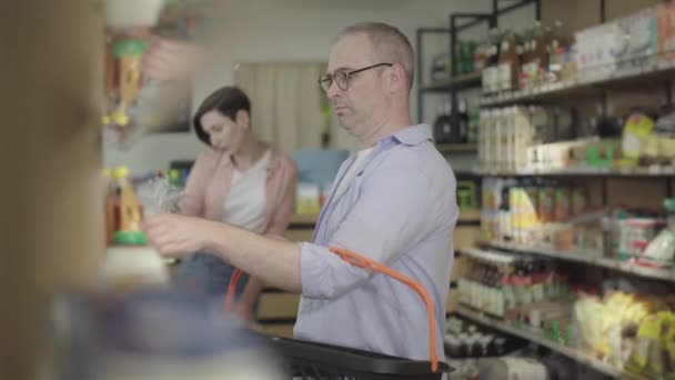 Handsome man scanning tomato paste with smartphone. Side view portrait of confident guy in eyeglasses checking goods in grocery using modern technologies. Lifestyle, buying, purchasing. — Stock Video