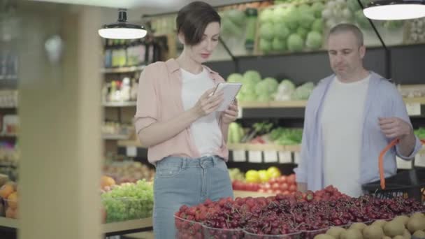 Θετικός Καυκάσιος άντρας και γυναίκα αγγίζουν τα χέρια κατά λάθος καθώς παίρνουν φράουλα από το ράφι του σούπερ μάρκετ. Πορτρέτο του γελώντας αρσενικό και θηλυκό πελάτη αγοράζουν τρόφιμα στο παντοπωλείο. Τρόπος ζωής, φλερτ. — Αρχείο Βίντεο