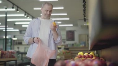 Beyaz adam markette domates seçiyor. Gülümseyen yetişkin alıcının portresi plastik torbaya sebze koyuyor. Diyet, vejetaryenlik, sağlıklı beslenme, yaşam tarzı..