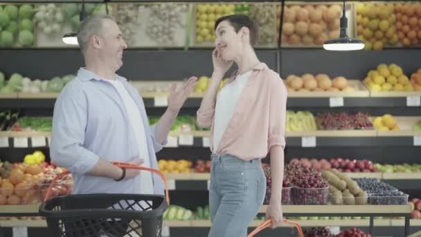 Charmante jonge vrouw flirtend met volwassen blanke man in de supermarkt. Zijaanzicht portret van een positief stel dat in de supermarkt praat. Lifestyle, liefde op het eerste gezicht, flirten. — Stockvideo