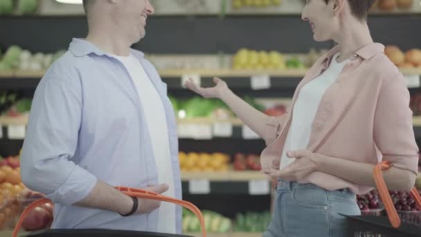 Unrecognizable young woman flirting with man in grocery. Side view of Caucasian brunette stylish lady talking to guy she likes in food shop. Lifestyle, flirt, coquette, consumerism. — Stock Video