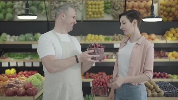 Consultor sorrindo dando cesta de cereja doce para charmoso cliente feminino. Mulher branca bonita nova que compra frutas deliciosas no supermercado. Felicidade, consumismo, estilo de vida . — Vídeo de Stock