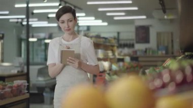 Not defteriyle marketteki raflara bakıp not alan kendine güvenen beyaz bir kadın. Yiyecek dükkanında eşyaları kontrol eden pozitif kadın işçinin portresi. Ticaret, endüstri, tüketim, tazelik.