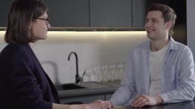 Gözlüklü, erkek arkadaşıyla konuşan ve gülümseyen neşeli esmer adamın yan görüntüsü. Neşeli, mutlu, beyaz eşcinsel çiftin evde sohbet edişinin portresi. Boş zaman, lgbt yaşam tarzı, kaynaşma.