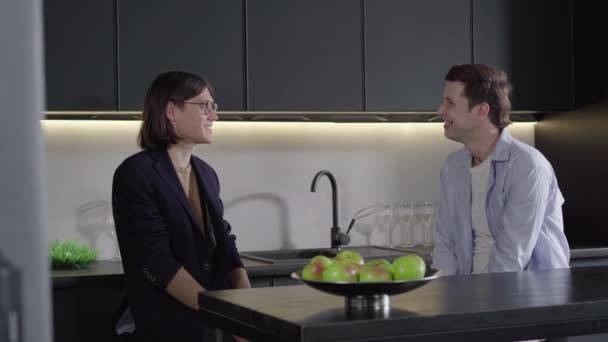 Dos gays caucásicos felices hablando en la cocina y sonriendo. Retrato de pareja del mismo sexo charlando en casa dentro. Familia del mismo sexo disfrutando los fines de semana juntos. Vinculación, amor, estilo de vida . — Vídeo de stock