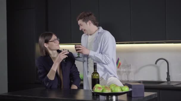 En positiv brunett som skålar för pojkvännen i köket. Kameran närmar sig glada kaukasiska homosexuella par firar årsdagen. Glädje, lgbt livsstil, fritid, lycka. — Stockvideo