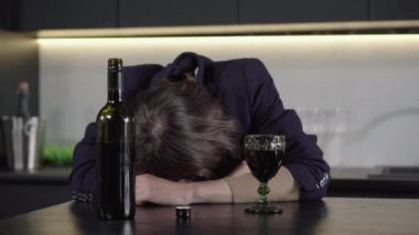 Şarap şişesiyle masada uyuyan tanınmayan esmer adamın yakın çekimi. Kafkasyalı alkolik, genç, bilinci kapalı bir evin portresi. Alkol bağımlılığı, bağımlılık, alkolizm.
