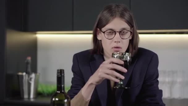 Porträtt av deprimerad brunett man i glasögon dricka vin från glas och faller på bordet. Ung berusad kaukasisk kille som förlorar medvetandet på grund av alkoholmissbruk. Alkoholism, missbruk. — Stockvideo
