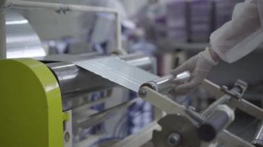Fabrika işçisi bitmiş ürünü makineden alıyor. Tanımlanamayan beyaz kadın üretim bandında çalışıyor alüminyum folyo üretiyor. Üretim, endüstri, iş.
