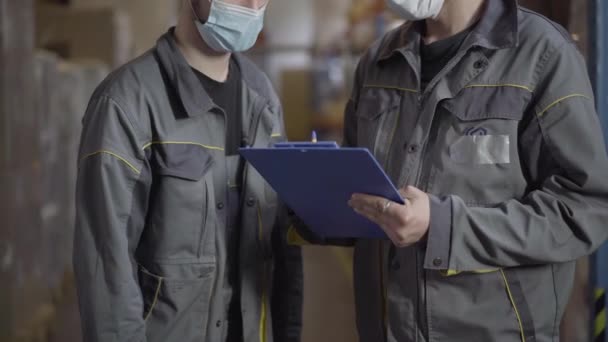 Onherkenbare mannen in het gezicht maskers schudden handen na het ondertekenen van vervoersdocumenten. Blanke mannelijke werknemers passeren de landings- en vertrekbrief. Coronavirus logistiek. — Stockvideo