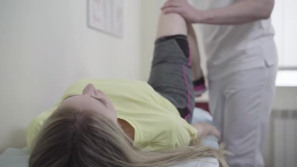 Mladá běloška ležící na pohovce na lékařské prohlídce jako nepoznatelná lékařka kontrolující trauma nohy. Nešťastná žena konzultační traumatolog v nemocnici po zranění. — Stock video