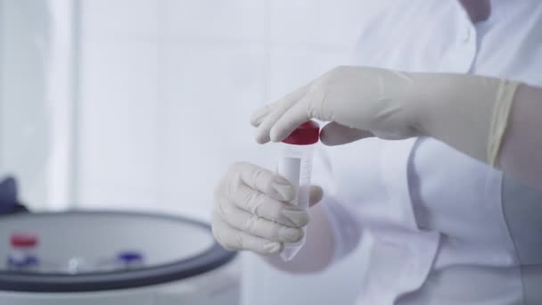 보호용 장갑을 끼고 빈 플라스크를 원심분리기에 넣는 여성 손. 알 수없는 캅카스 의사가 코비 디 우스 -19 전염병에 대한 혈액 검사를 연구실에서 하고 있습니다. 코로나 바이러스 백신 개발. — 비디오