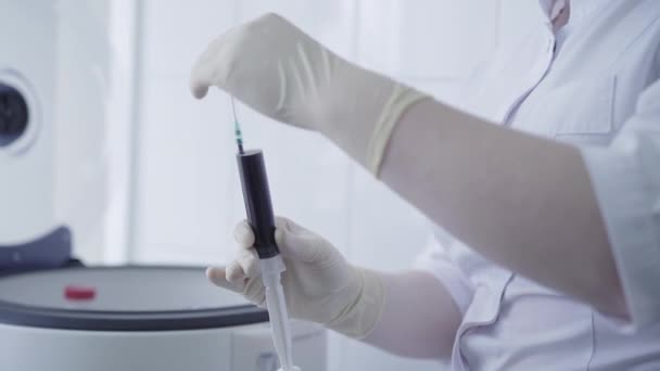 Eine unkenntliche Krankenschwester in Handschuhen und weißem Arztkittel öffnet eine Spritze, die mit Blut gefüllt ist. Laborassistentin untersucht Probe im Labor auf Covid-19 Pandemie. Entwicklung eines Impfstoffs gegen Coronavirus. — Stockvideo