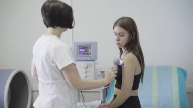 Esmer, beyaz romatolog hastanede kadın hastaya ultrason yapıyor. Tıbbi klinikte genç, zayıf bir kadını tedavi eden profesyonel bir doktorun yan görüntüsü..