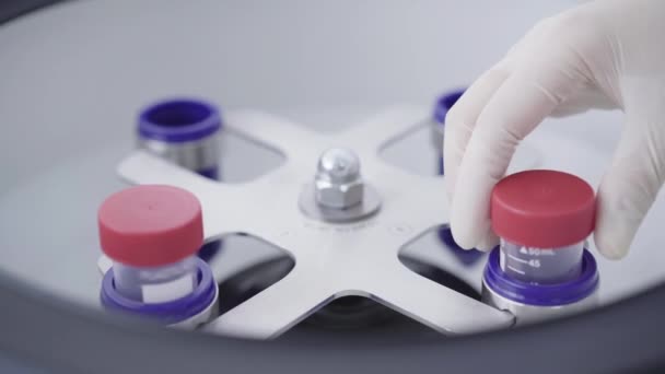 Female hand in gloves taking out flask with processed blood sample from centrifuge. Close-up of unrecognizable lab assistant working in laboratory. Coronavirus vaccine, Covid-19 pandemic. — Stock Video