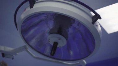 Arka planda beyaz bir erkek, öndeki cerrahi lambayı yakıyor. Hastane veya klinikteki ameliyathanede tıbbi ekipmanların yakılması.