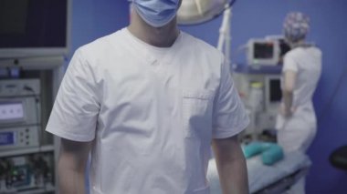 Ameliyat odasında el ele tutuşan maskeli tanınmayan bir doktor. Arka planda bulanık asistan ayarlama ekipmanları. Covid-19 salgınında hastanede çalışan cerrah ve hemşire..