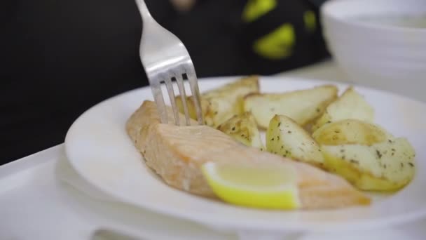 Extreme Nahaufnahme von rotem Fisch und Bratkartoffeln auf dem Tablett der Krankenstation. Unerkennbare kaukasische Frau, die mit Gabel Scheibe für Scheibe zu sich nimmt. Patientin ernährt sich in Klinik gesund. — Stockvideo