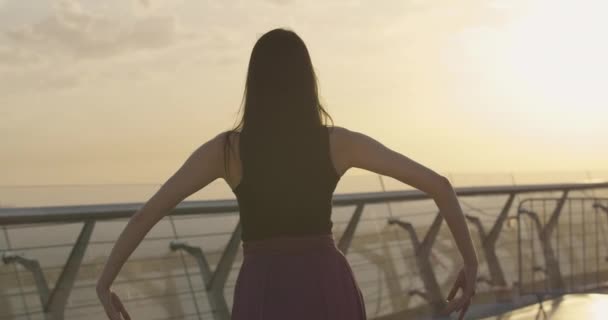 На тлі помаранчевого сходу чи заходу сонця з "являється витончена балерина. Молода кавказька балерина танцює просто неба на мості. Повільніше. Фільм 4k ProRes HQ. — стокове відео