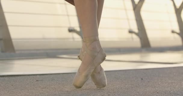 Slanke vrouwelijke blanke benen in punten die op tenen staan. Onherkenbare ballerina dansend op de brug bij zonsopgang op zomerdag. Klassiek ballet, choreografie. Cinema 4k ProRes Hoofdkwartier. — Stockvideo