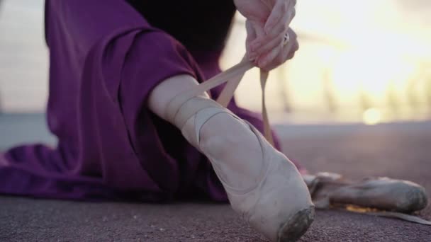 Close-up of female ballet dancer tying up pointe shoes. Unrecognizable young slim Caucasian ballerina putting on pointes at sunrise outdoors. Dancing lifestyle, choreography, elegance. — Stock Video