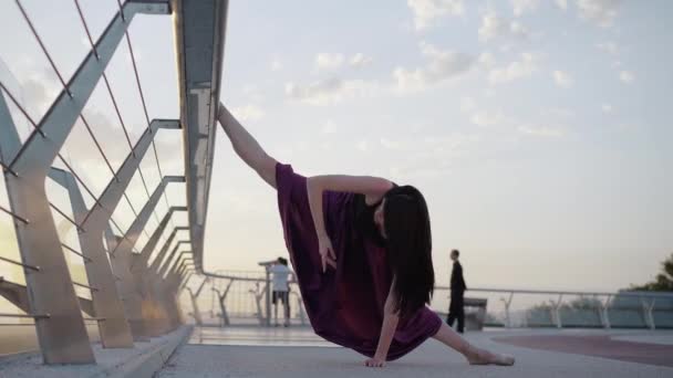 Amplio plano de elegante joven bailarina caucásica de pie dividida en puente y levantando la mano. Retrato de bailarina de ballet profesional que se entrena al aire libre al amanecer o al atardecer. Elegancia, estilo . — Vídeos de Stock