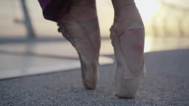 Збільшення жіночих ніг в точкових туфлях, що йдуть по асфальтному мосту на світанку або заході сонця. Невпізнавана кавказька балерина танцює надворі в літній день. Ґрейс, елегантність, спосіб життя.. — стокове відео