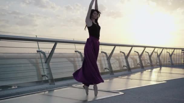 Elegante bailarina caucasiana girando em dedos do pé na ponte pela manhã. Retrato de tiro largo de dançarina de balé jovem confiante praticando dança ao nascer do sol ao ar livre. Elegância, feminilidade, coreografia . — Vídeo de Stock