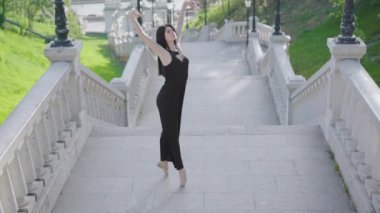 Parmak uçlarında yürüyen, dizlerinin üstüne çöküp bükülen büyüleyici genç balerin manzarası. Şehir merkezinde merdivenlerde klasik bale hareketleri yapan profesyonel bir dansçı..