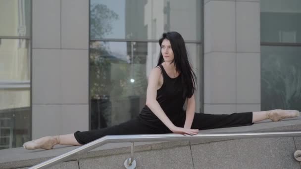 Slim elegáns nő ül split a városi lépcsőn, és előrehajolt. Portré fiatal gyönyörű barna balerina edzés a városban a nyári napon. Kaukázusi női balett táncos a szabadban. — Stock videók