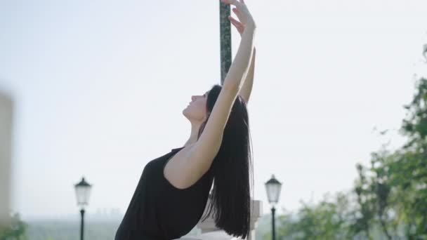 Mulher branca morena bonita dobrando sobre corrimãos escadas no dia ensolarado. Vista lateral retrato de bailarina jovem dançando na cidade. Câmera segue o movimento da dançarina de balé feminina encantadora . — Vídeo de Stock