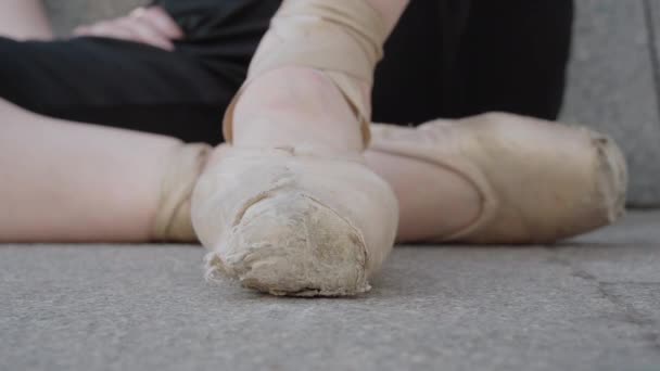 Extreme κοντινό πλάνο του γυναικείου ποδιού σε σημεία που στέκονται στις μύτες των ποδιών. Άγνωστη λευκή χορεύτρια μπαλέτου που κάθεται στην άσφαλτο της πόλης. — Αρχείο Βίντεο