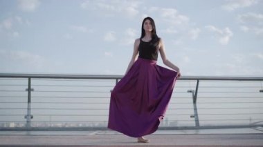 Kendine güvenen ciddi balerin tek ayağının üzerinde duruyor ve ayağını kaldırıyor. Güneşli yaz gününde klasik bale yapan beyaz bir kadının geniş açılı portresi..