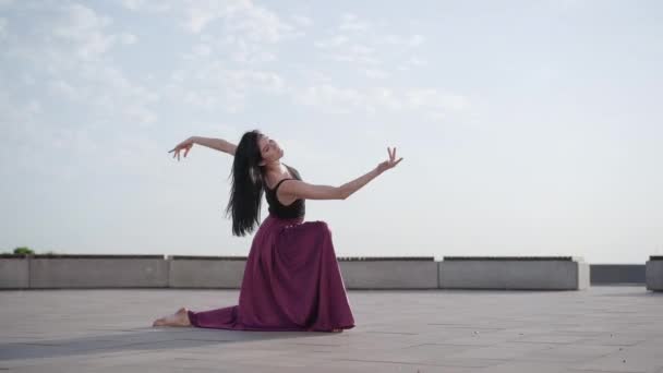 Ampla dose de dançarina de balé graciosa sentada em um joelho e se movendo. Retrato de bela bailarina caucasiana elegante dançando ao ar livre no dia ensolarado. Mulher encantadora na praça da cidade . — Vídeo de Stock