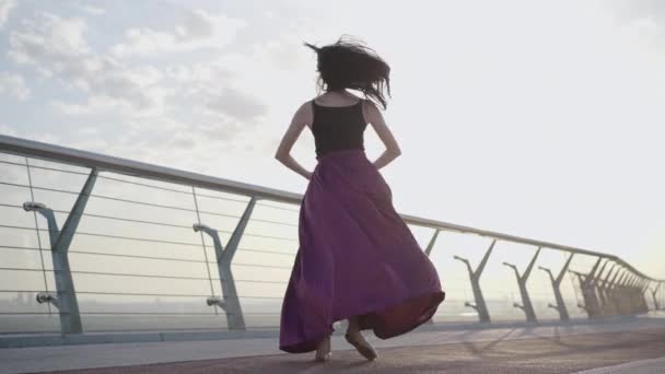 Портрет упевненої професійної балерини, що виконує класичний танцювальний рух на мості на світанку. Широкий постріл елегантної кавказької жінки, що танцює на вулиці влітку. Краса, хореографія. — стокове відео