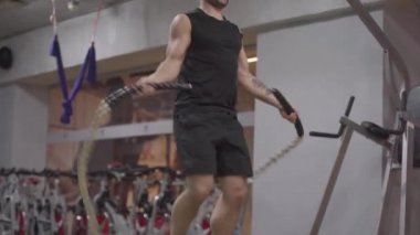 Spor salonunda ip atlayan genç beyaz tenli sporcu. İçeride spor envanteri olan, kendine güvenen erkek vücut geliştirici eğitiminin portresi. Özgüven, yaşam tarzı, dayanıklılık.