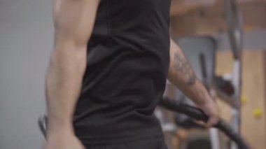 Yakın plan, kendine güvenen güçlü sporcu spor salonunda ip atlıyor. Canlı kamera spor kulübünde antrenman yapan beyaz tenli bir erkek vücudu boyunca hareket ediyor. Dayanıklılık, vücut geliştirme, spor.