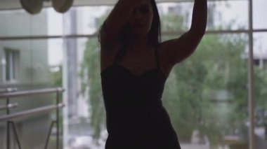 Büyük pencerenin önüne doğru ilerleyen beyaz tenli kadın dansçının ön görüntüsü. Kamera, spor salonunda striptiz yapan genç bir kadının muhteşem vücudu boyunca hareket ediyor. Dans, yaşam tarzı, spor.