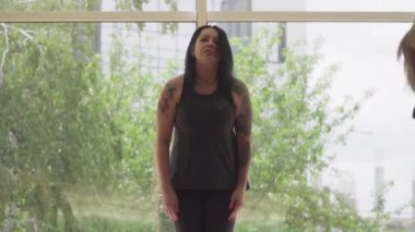 Kamera, kendine güvenen kadın yoga eğitmenini ayakta el kaldırırken takip ediyor. Ellerinde dövmeleri olan, spor salonunda asana öğreten yetişkin beyaz kadın portresi. Zen, yaşam dengesi, yaşam tarzı.