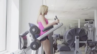 Spor kulübünde ekipman üzerinde egzersiz yapan çekici sarışın bir sporcunun geniş açılı çekimi. Beyaz tenli genç bir kadının bacak kaldırma ve kas çalıştırma portresi. Spor, yaşam tarzı, güzellik.