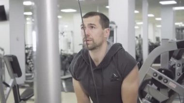 Spor aletlerini spor salonunda kullanan beyaz tenli bir sporcunun portresi. Genç esmer sakallı adam el kaslarını çalıştırıyor, ağırlık sayımını kaldırıyor. Erkeklik, atletizm, yaşam tarzı.
