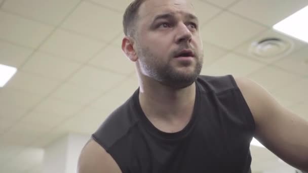 Close-up portret van geconcentreerde jonge sportman training handspieren. Zelfverzekerde blanke brunette die gewichten optilt in de sportschool. Begrip sport, mannelijkheid, uithoudingsvermogen. — Stockvideo